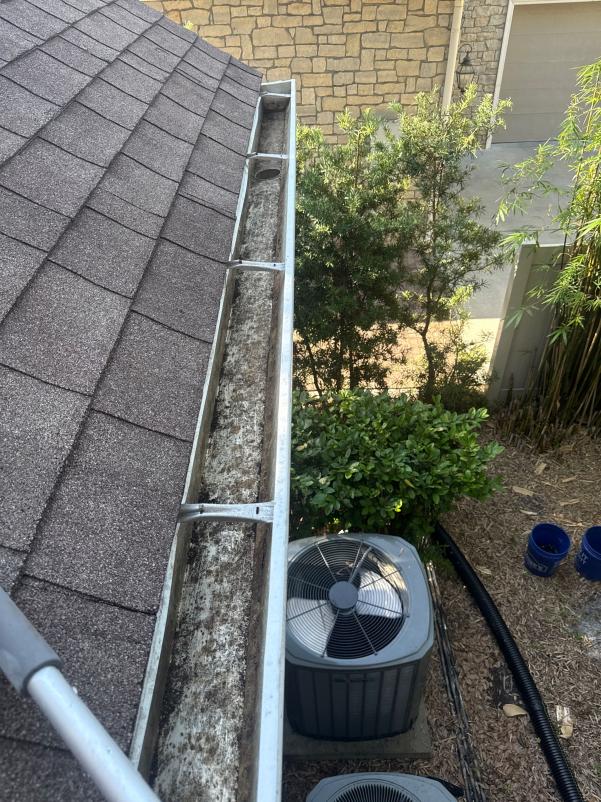 gutter cleaning service showing a dirty gutter clogged with leaves and debris near air conditioning unit and landscaping