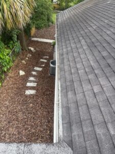 cleaning gutters along the edge of a roof with surrounding landscaping and a visible air conditioning unit