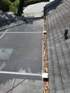 gutter cleaning service removing debris from a roof outfitted with screens and shingles showing accumulated leaves and dirt