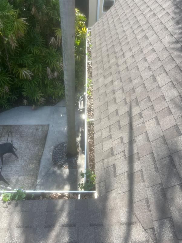 gutter cleaning service removing debris from gutters on a sloped roof near some greenery and a patio area