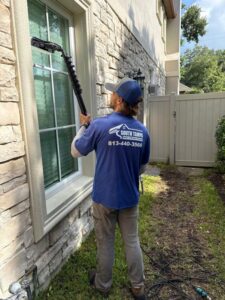 a worker from south tampa gutter and window cleaning using a pole to clean windows on a house