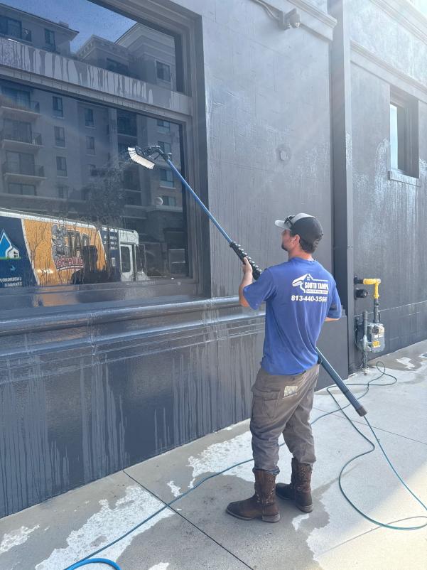 man cleaning windows with a long pole water flowing down wall and equipment placed nearby on the ground
