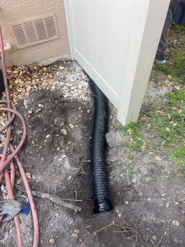 black drainage pipe installed near a fence with exposed soil and gravel around the area