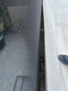 cleaning gutter and window area with debris visible on the edge and a person wearing a shoe in the corner