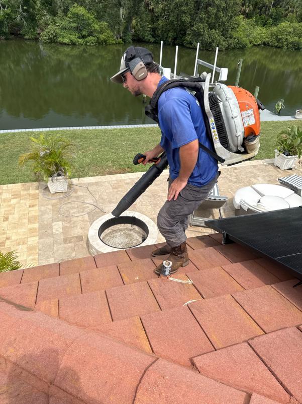 man using a leaf blower on a roof to clear debris near a circular drain by the water