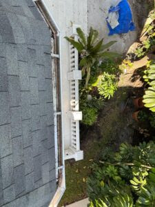 gutter cleaning along a sloped roof with vegetation and pavers visible in the surrounding area