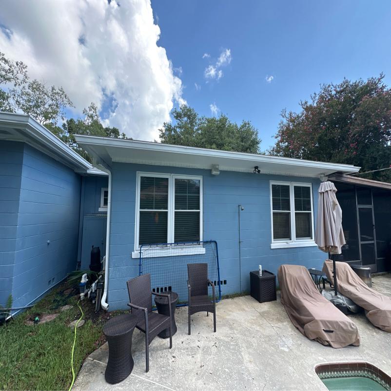 cleaning service for blue house exterior showing windows patio furniture and surrounding greenery with cloudy sky in background