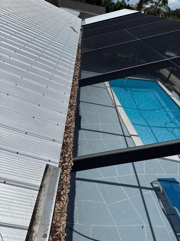 gutter cleaning service performed near a swimming pool with a screened enclosure and concrete patio area visible below