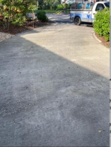 a concrete driveway showing signs of dirt and debris with a service vehicle parked nearby and lush greenery around