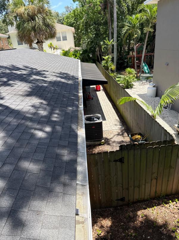 gutter cleaning service on a house roof with a clear view of the surrounding yard and patio area