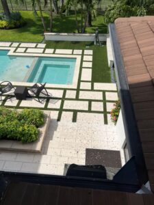 cleaning debris from patio tiles and pool area with landscaped garden visible in background