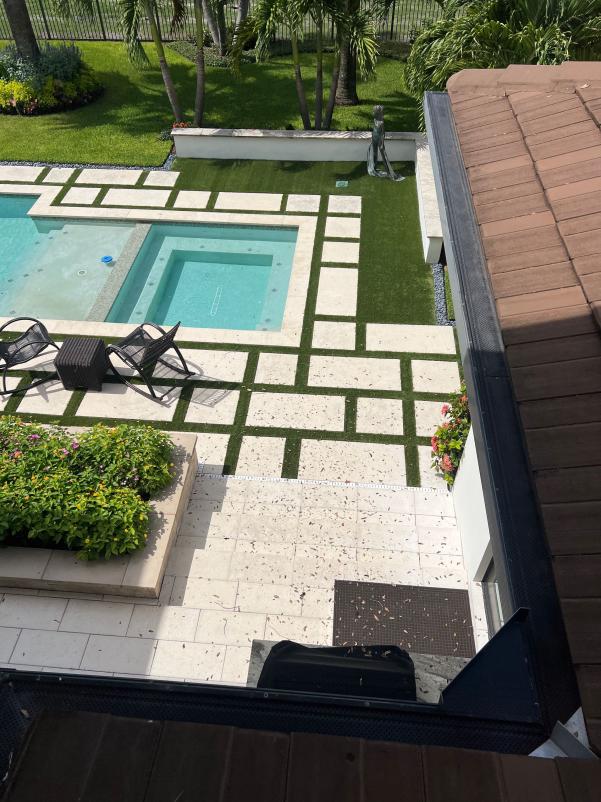 cleaning debris from patio tiles and pool area with landscaped garden visible in background