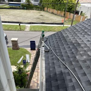 gutter cleaning services being prepared with a ladder and hose positioned on a gray shingle roof with tools visible