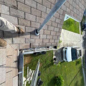 gutter cleaning in progress with ladder and equipment visible rooftops and grass in view