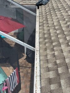 cleaning of a gutter showing debris buildup with a view of a roof and a screened enclosure in a backyard