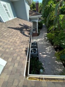 cleaning gutters with visible dirt and debris along the edge of a roof near air conditioning units and landscaping