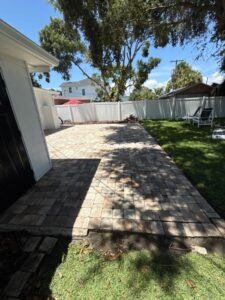 paver patio installation in a backyard with green grass and a white fence surrounding the area