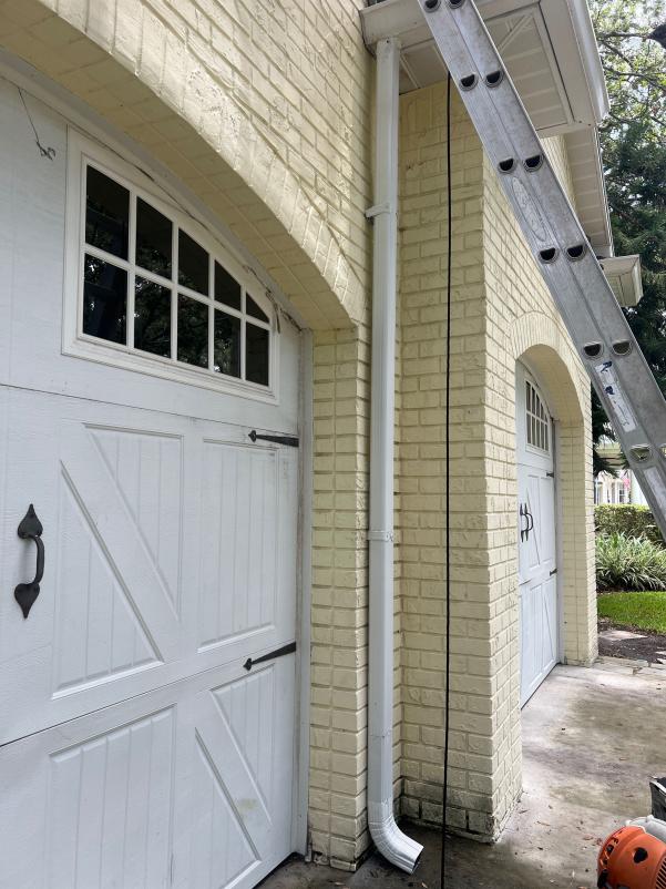 cleaning of a yellow brick wall and gutters with a ladder positioned against the structure
