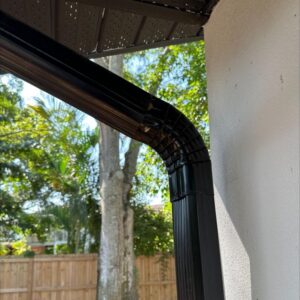 black downspout from a gutter system connected to a house with trees and a wooden fence in the background