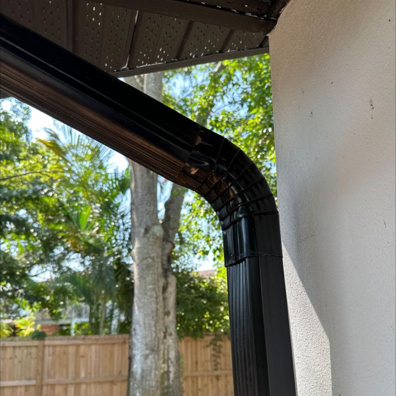 black downspout from a gutter system connected to a house with trees and a wooden fence in the background