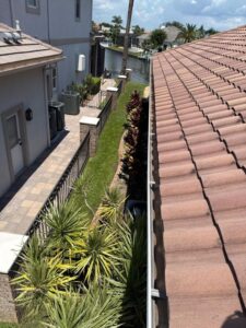gutter cleaning and maintenance on a residential roof with a clear view of landscaping and a waterway nearby