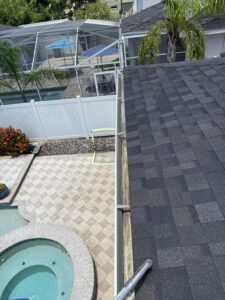 rooftop view showing a clean black shingle roof near a swimming pool and patio area with landscaping and a privacy fence