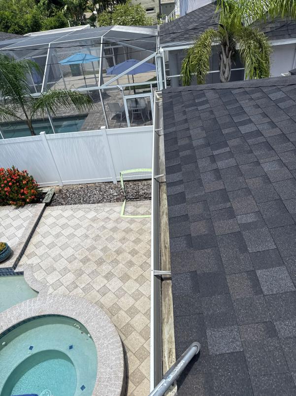 rooftop view showing a clean black shingle roof near a swimming pool and patio area with landscaping and a privacy fence