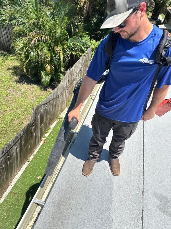gutter cleaning service using a vacuum system to remove debris from the roof edge near a palm tree and fence