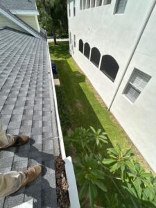 gutter cleaning in progress showing a person standing on a roof with leaves and debris visible in the gutter