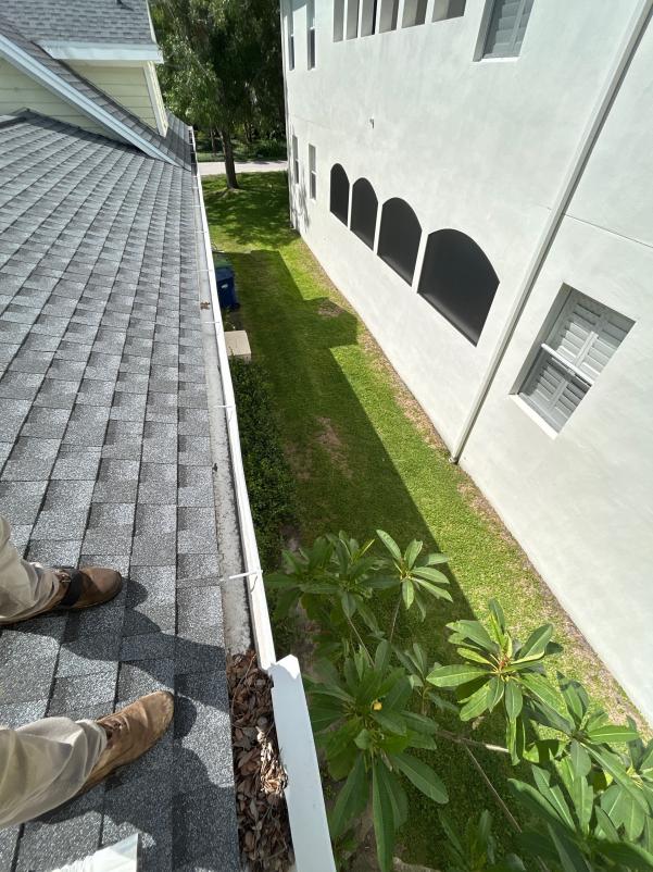 gutter cleaning in progress showing a person standing on a roof with leaves and debris visible in the gutter