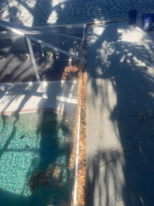 gutter cleaning with debris and leaves accumulated near a pool area additional shadows and sunlight visible on surfaces