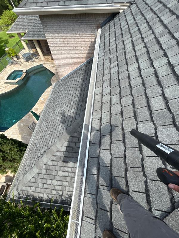 cleaning gutters on a sloped roof using a blower tool with a view of a pool and landscaping below