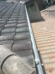 gutter cleaning service on a roof with tile shingles showing debris and dirt accumulation on the roof surface