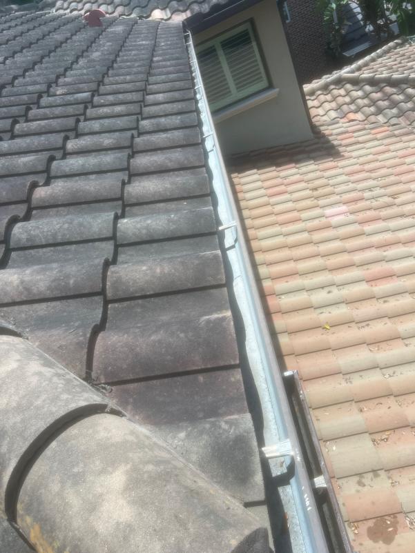 gutter cleaning service on a roof with tile shingles showing debris and dirt accumulation on the roof surface