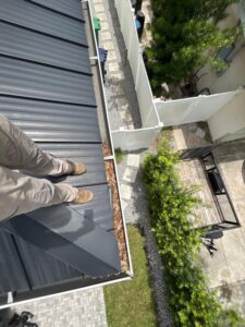 cleaning leaves and debris from a metal roof standing on the edge of the roof with a clear view of the yard