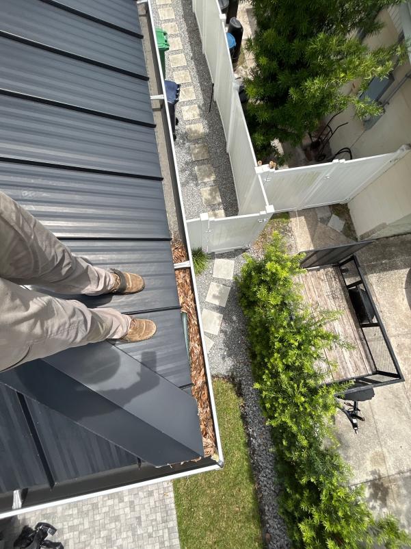 cleaning leaves and debris from a metal roof standing on the edge of the roof with a clear view of the yard