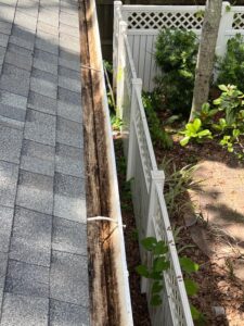 gutter cleaning showing buildup of dirt and debris along the edge of the roof adjacent to a garden and fence