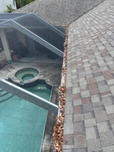 cleaning gutters filled with leaves near a roofline above a pool area with a hot tub visible