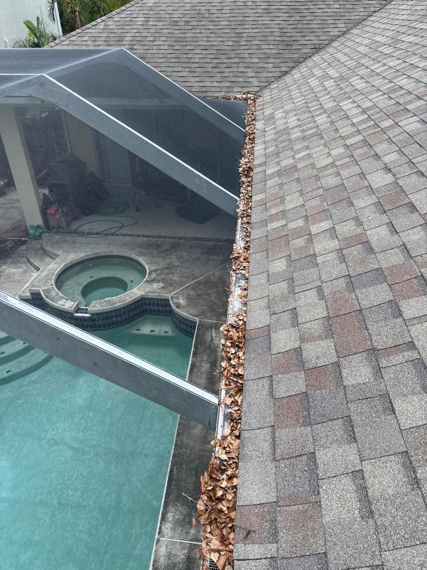 cleaning gutters filled with leaves near a roofline above a pool area with a hot tub visible