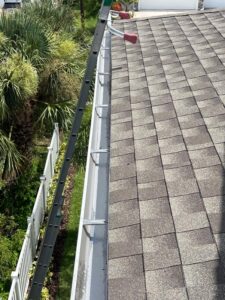 gutter cleaning in progress with a ladder positioned against a house near a roof and lush greenery surrounding the area