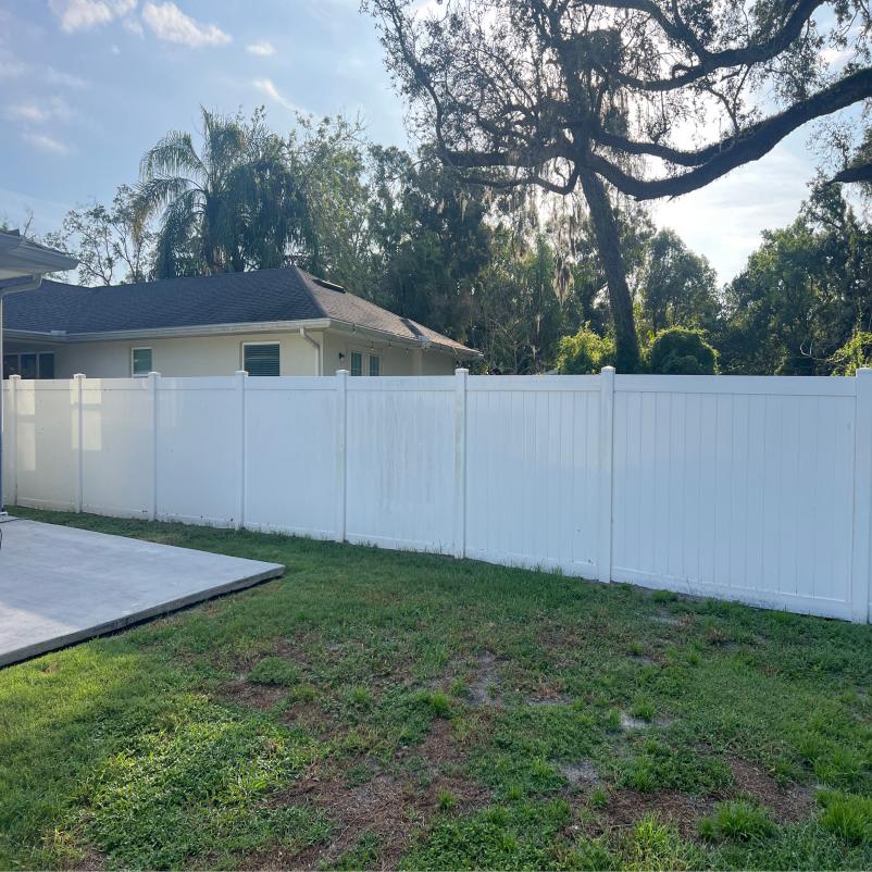 the image depicts a residential backyard with a white vinyl fence and green grass possibly prepared for maintenance or cleaning services