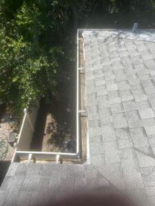 gutter cleaning with debris accumulation visible on a roof edge alongside trees and a fenced yard area