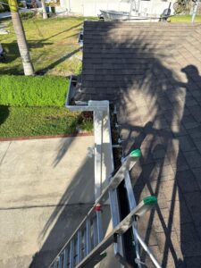 gutter cleaning service with a ladder positioned on a roof near the edge and clear view of the surrounding area