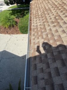 gutter cleaning service revealing debris on a sloped rooftop with a shadow showing an individual taking a photo