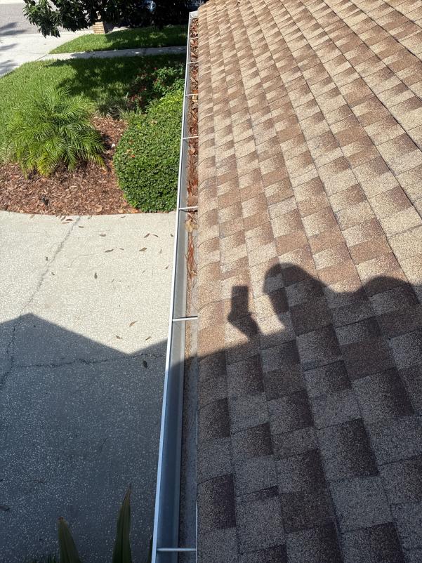 gutter cleaning service revealing debris on a sloped rooftop with a shadow showing an individual taking a photo