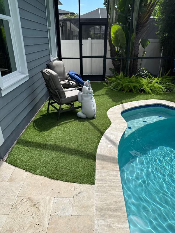 patio area with artificial grass a poolside chair and a decorative figure near the pool surrounded by greenery