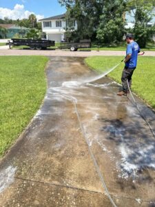 a worker pressure washing a concrete driveway with soap and water showing a portion cleaner than the surrounding areas