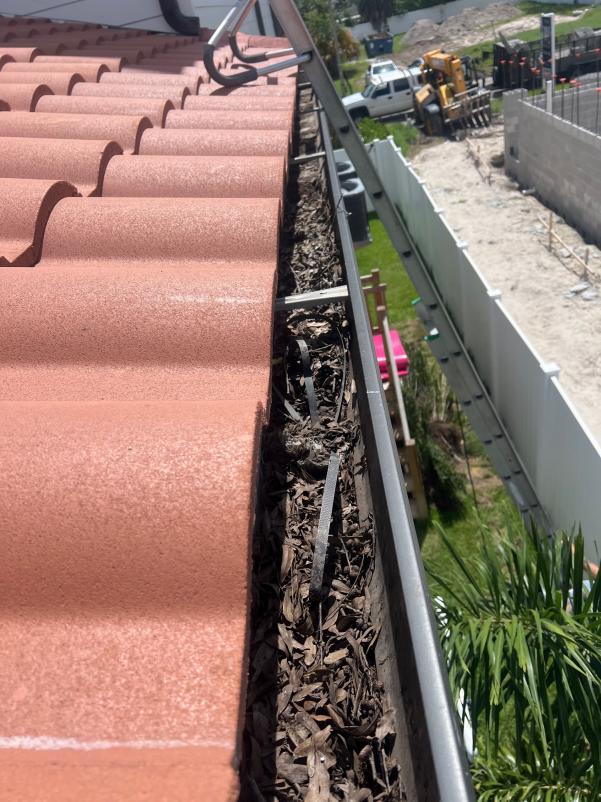 gutter cleaning showing accumulated leaves and debris in a residential gutter near a terracotta roof