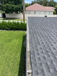 gutter cleaning near a gray shingled roof with visible debris accumulation and well-maintained green lawn in background
