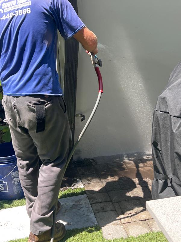 employee using a pressure washer to clean a surface near a wall and patio area